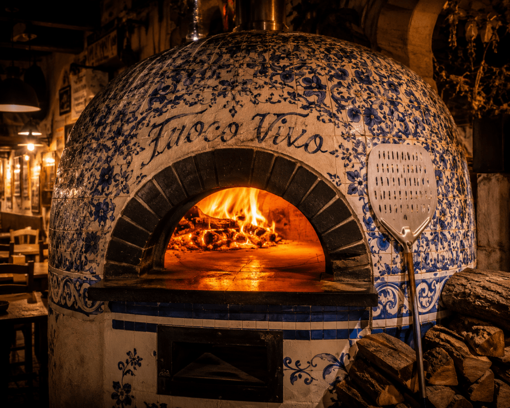 Photorealistic traditional Neapolitan wood-fired pizza oven at Fuoco Vivo with hand-painted Vietri ceramic tile facade flames inside the dome and Fuoco Vivo inscription above the arch
