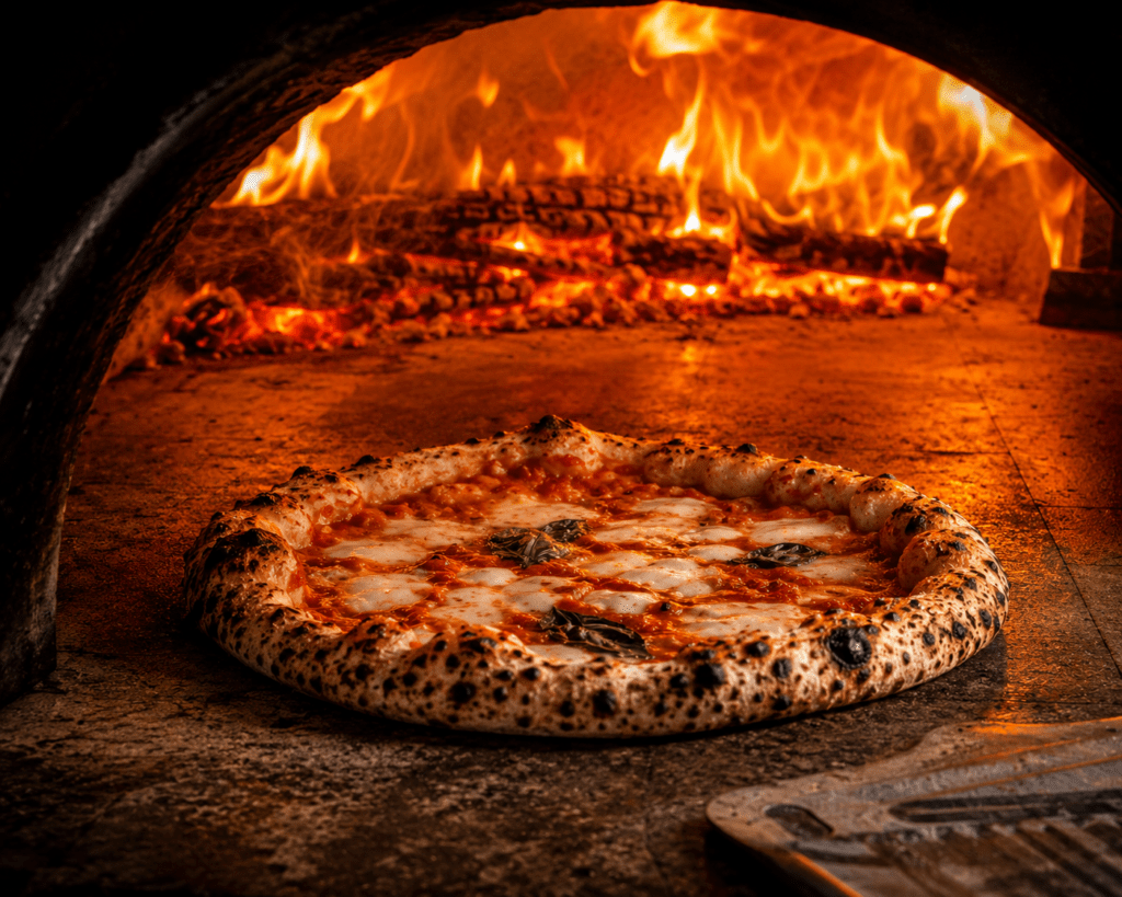 Photorealistic view inside Fuoco Vivo wood-fired oven showing Neapolitan pizza baking at 485 degrees with puffed charring cornicione bubbling San Marzano tomato melted Fior di Latte and active flames at dome rear